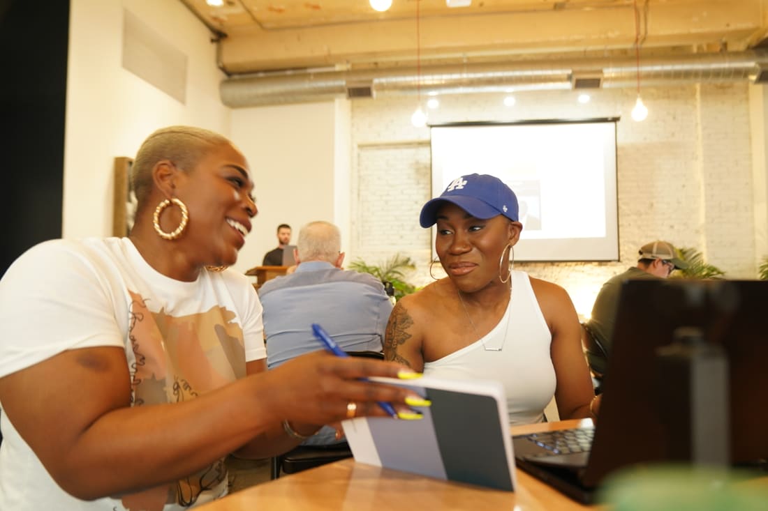 Color candid of Nikki laughing with a friend over a laptop at a community workshop