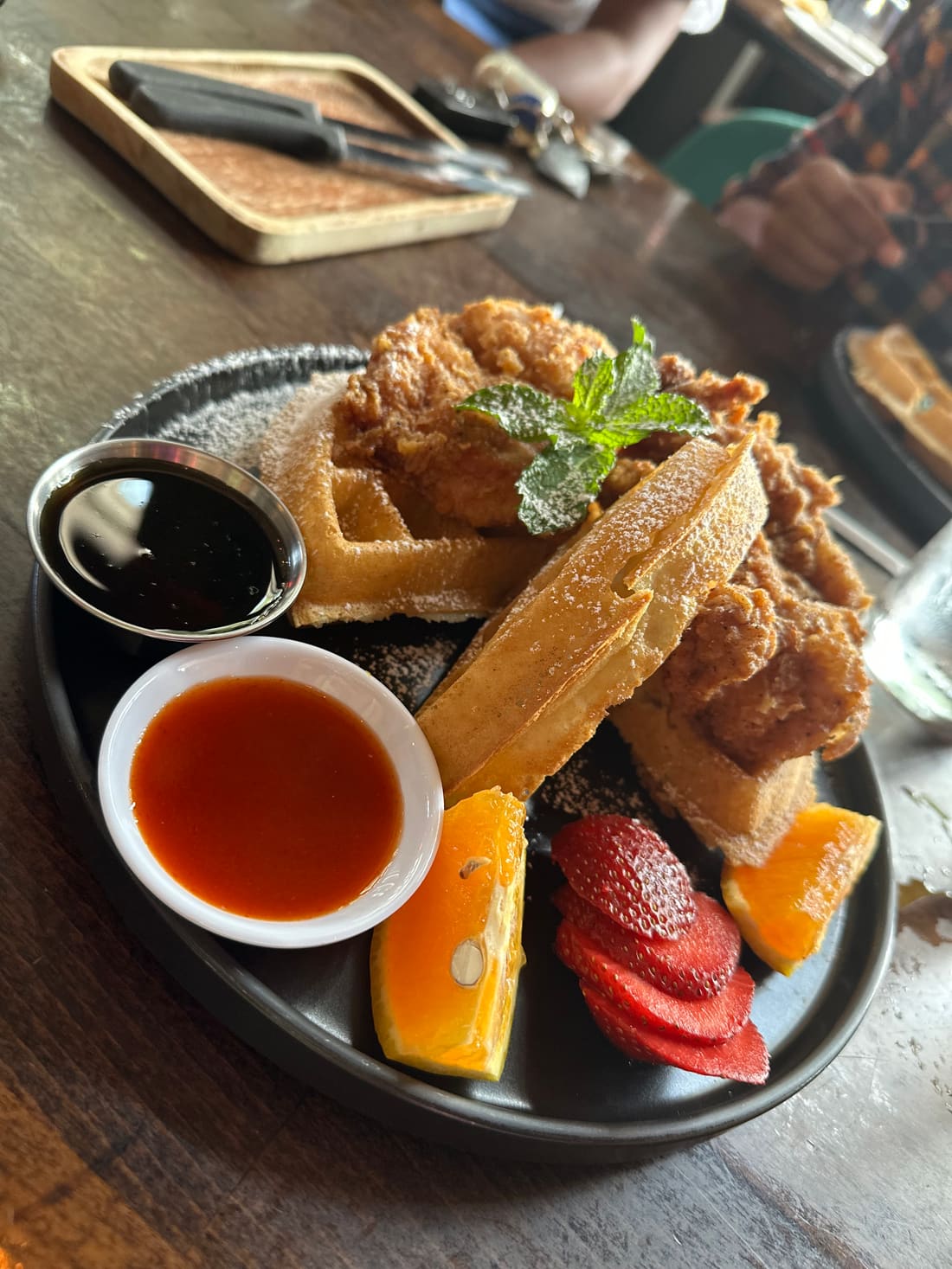 Color photo of a chicken and waffles brunch plate with fruit and syrup