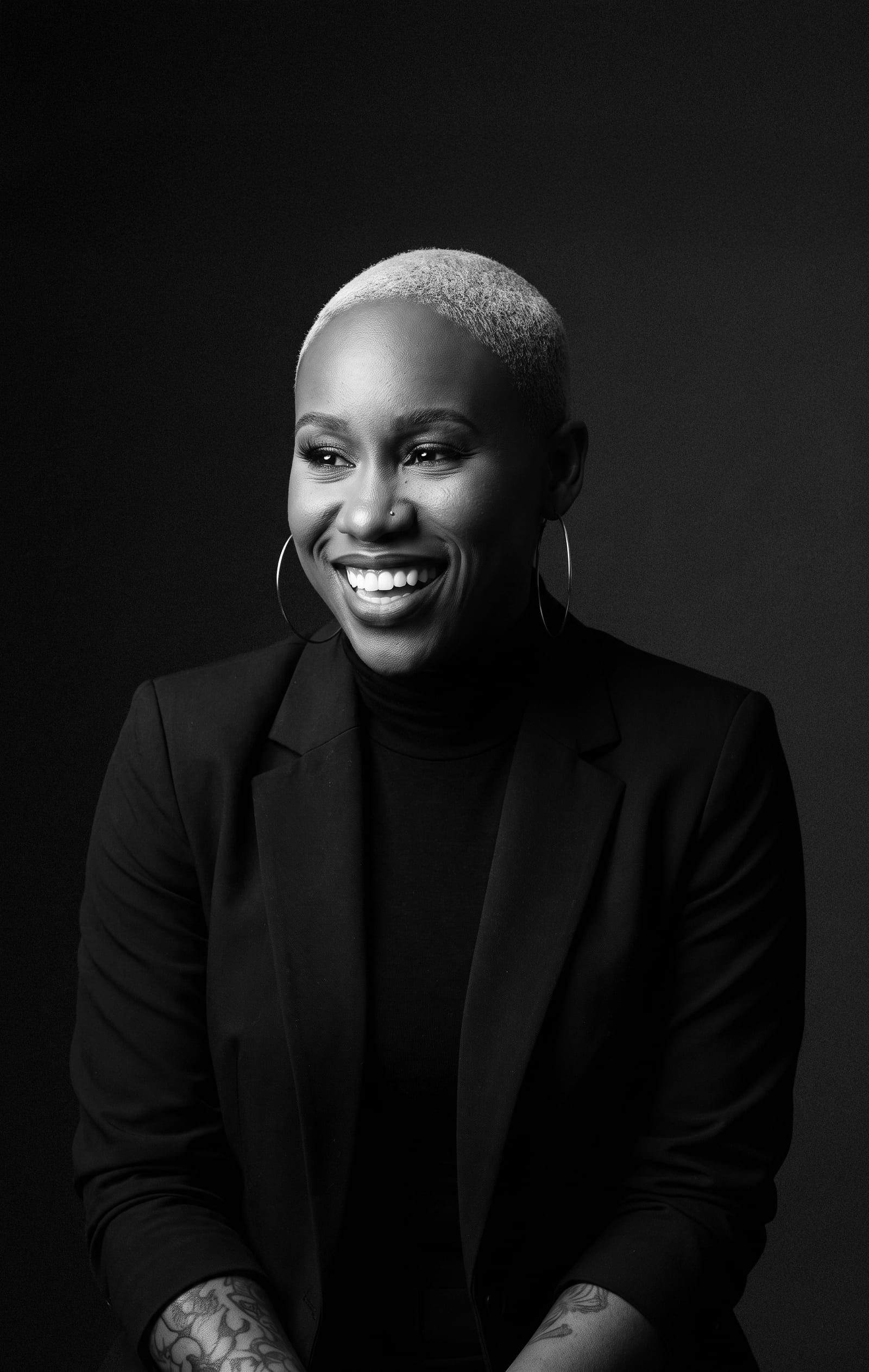 Black and white editorial portrait of Nikki Rumph smiling in a black blazer against a dark studio backdrop